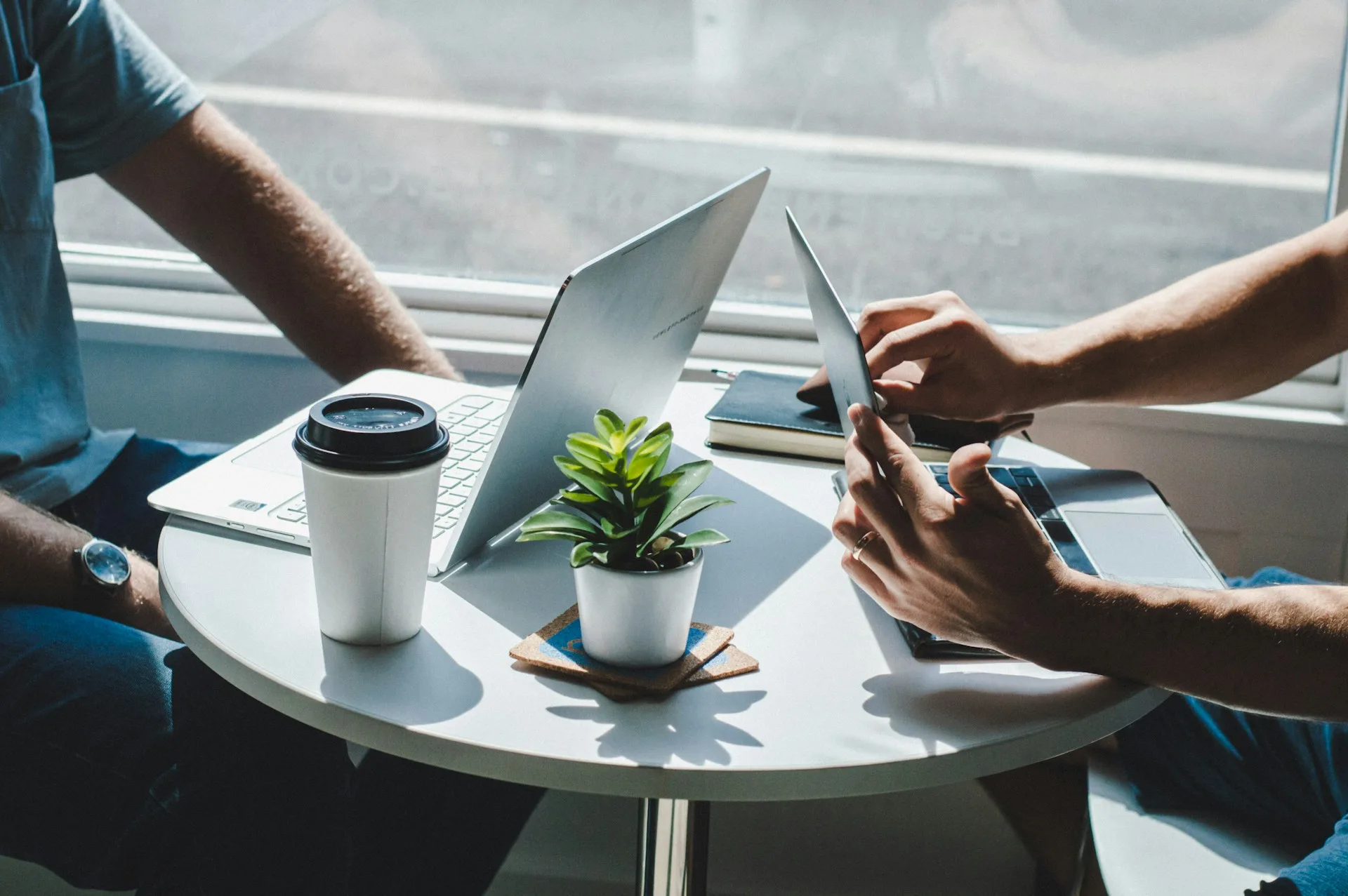 Two people talking on a table while use their laptops